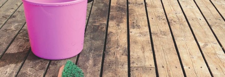 Ein pinker Eimer und eine Bürste auf einer Holzterrasse. 